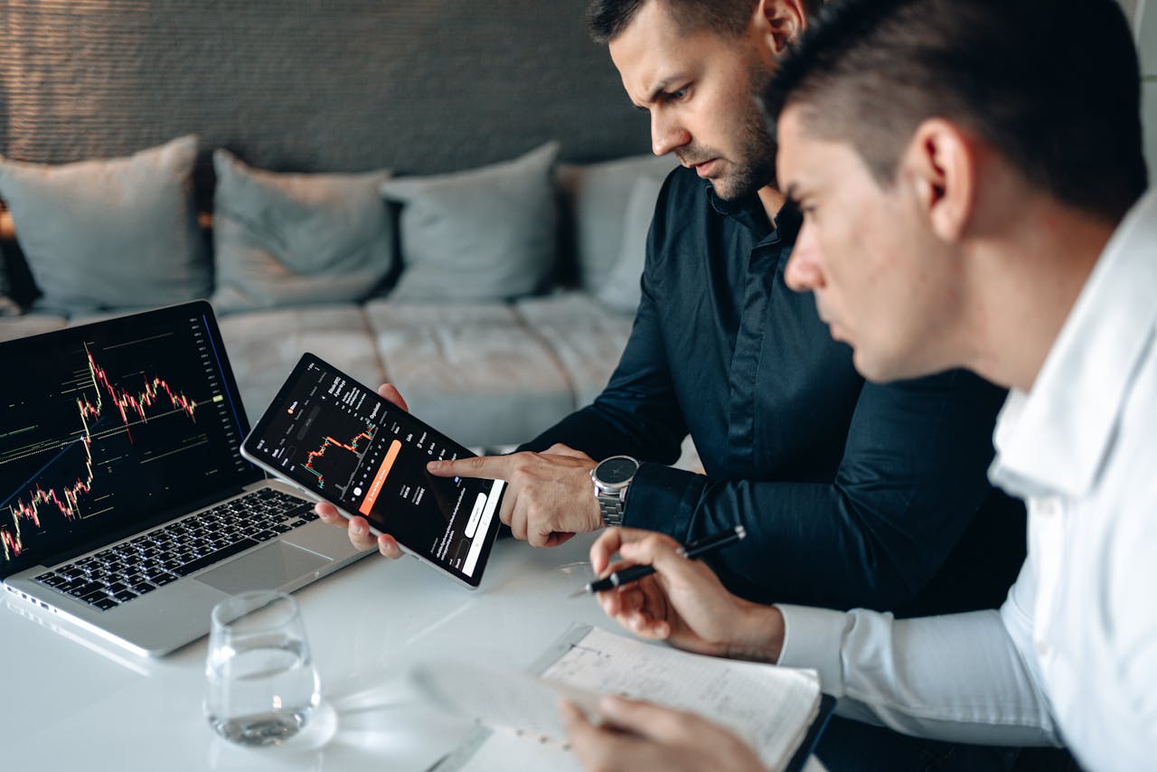 Two business professionals using a laptop and tablet to analyze online trading data indoors.